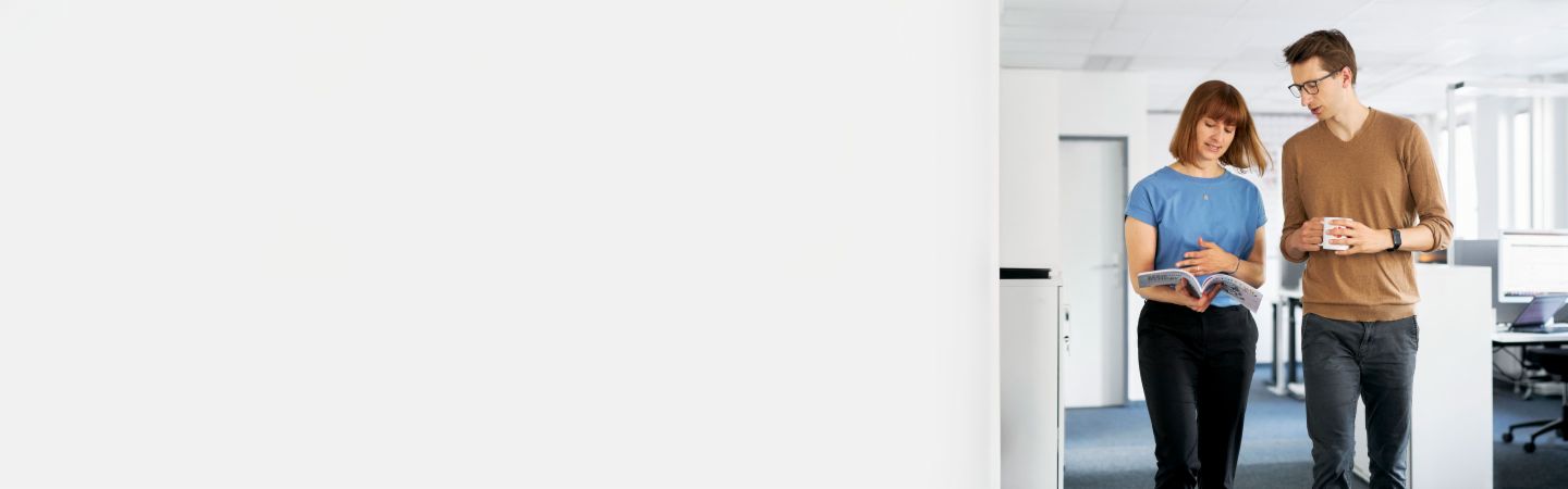 Deux collègues discutent dans un bureau moderne de la manière dont EOS peut protéger les entreprises contre les défauts de paiement et maximiser leur liquidité dans la gestion des créances, tandis qu'un autre employé travaille sur l'ordinateur en arrière-plan.