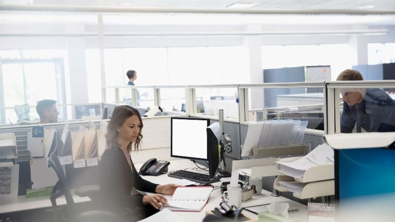 Numérisation: trois employés se trouvent dans un bureau open space, une femme est assise entre des papiers et son ordinateur
